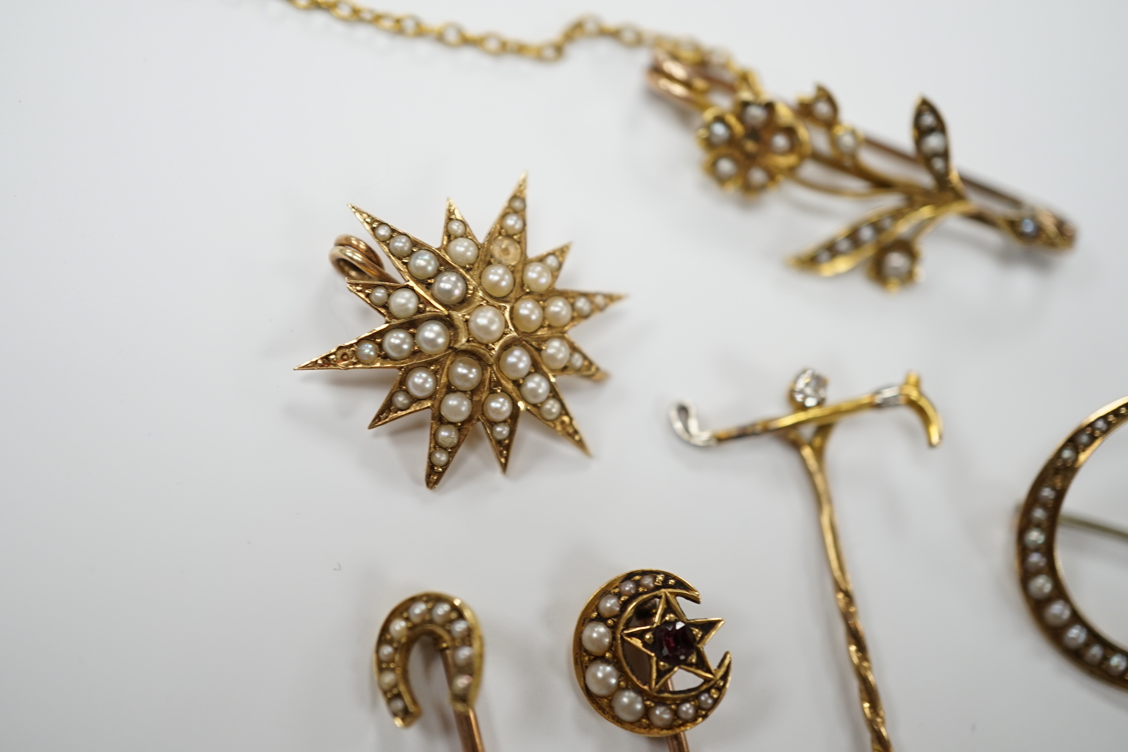 Three early to mid 20th century yellow metal and seed pearl set brooches, largest 34mm, two similar stick pins and a diamond set riding crop stick pin.